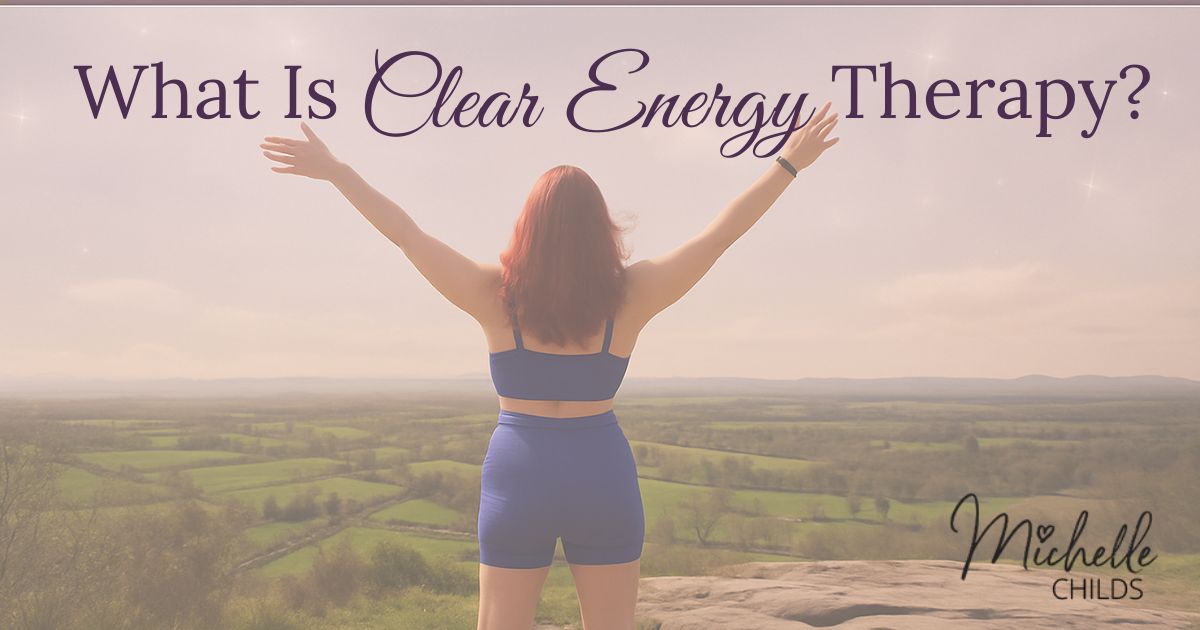 A woman with long red hair stands on a hilltop with arms raised, overlooking a scenic countryside landscape under a soft pink sky. Text at the top reads "What Is Clear Energy Therapy?" in elegant serif and script fonts. The bottom corner features the name Michelle Childs in a handwritten-style logo.